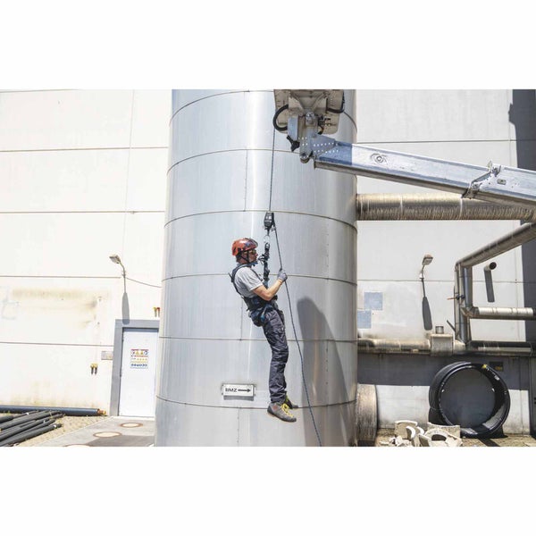 Person mit Absturzsicherung und Klettergurt bei Arbeiten an einem großen Metalltank im Außenbereich.