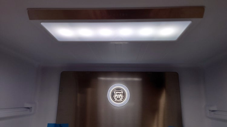 Innenraum eines Kühlschranks mit heller LED Beleuchtung und einer Metallrückwand mit beleuchtetem Kaiser Logo.