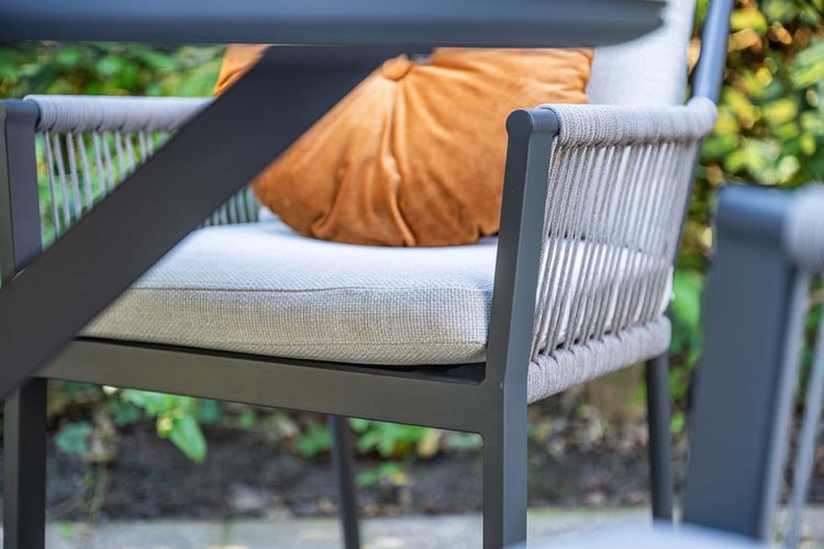 Detailansicht eines Gartenstuhls mit dunklem Metallgestell, Armlehnen mit Seilbespannung und einem hellen Sitzkissen.