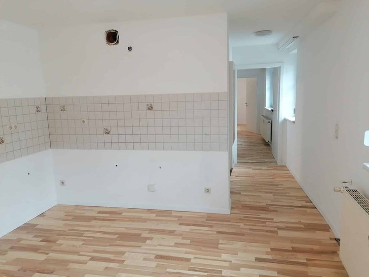 Heller Raum mit Parkettboden, weißer Innentür und einem Fliesenspiegel für eine Küchenzeile mit Wasseranschlüssen.