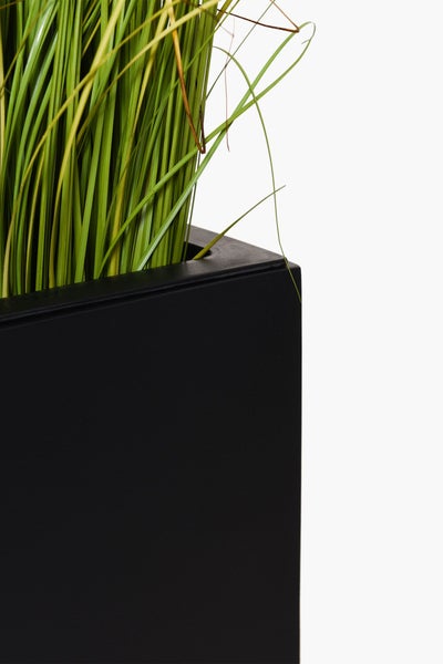 Detailansicht eines schwarzen rechteckigen Pflanzgefäßes mit künstlichem Gras.