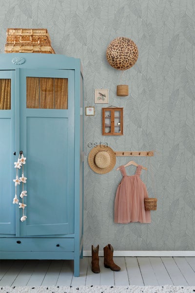 esta home Logo auf einer Vliestapete mit Blattmuster in einem hellen Zimmer mit einem blauen Schrank, Kleiderhaken und einem Kleid.
