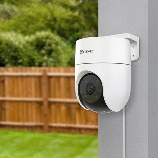 EZVIZ Überwachungskamera für den Außenbereich mit Schwenk- und Neigefunktion, montiert an einer Wand vor einem Garten mit Holzzaun.
