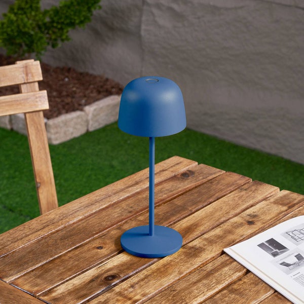 Blaue LED-Tischleuchte auf einem Holztisch im Garten in einer hellen, organisierten Außenumgebung mit Holzstuhl.