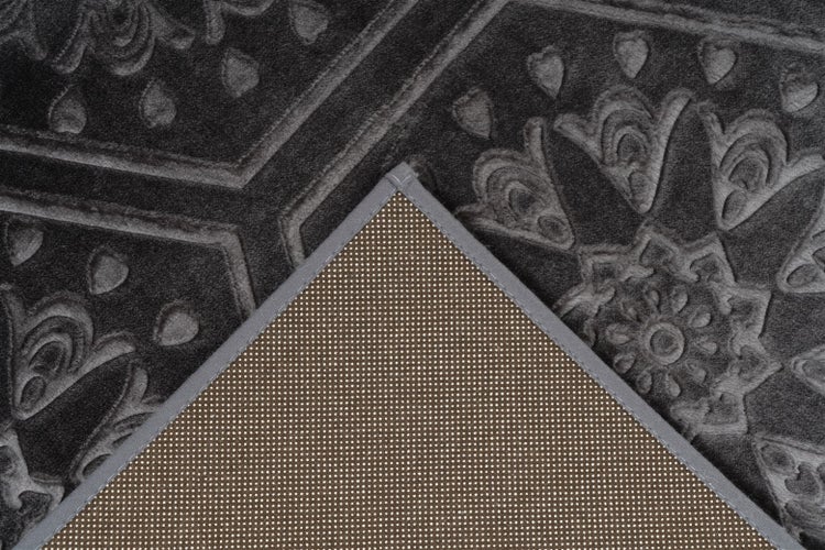 Nahaufnahme eines gemusterten Teppichs mit umgeschlagener Ecke, die die rutschhemmende Rückseite mit Noppenstruktur zeigt.