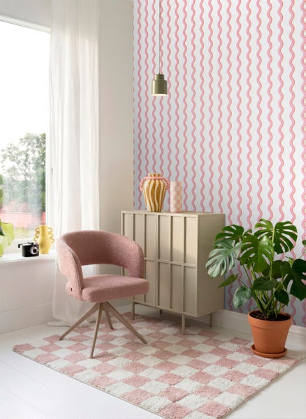 Tapete mit rosa und orangefarbenen Wellenlinien in einem modernen Wohnzimmer mit Sessel, Sideboard und Zimmerpflanze.