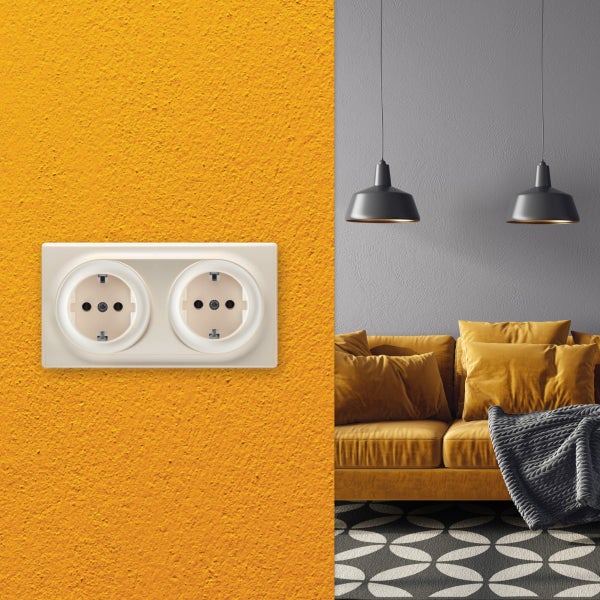 Doppelte Steckdose montiert auf einer strukturierten Wand neben einem Wohnbereich mit Sofa und Hängelampen.
