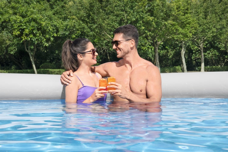 Ein Paar entspannt in einem aufblasbaren Pool im Garten und stößt mit Getränken an.