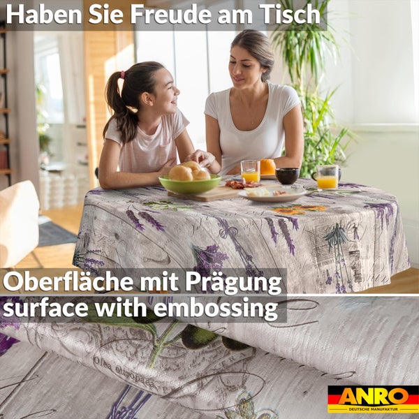 Rundes Wachstuch mit Lavendel- und Sonnenblumenmotiven auf einem Esstisch. Detailansicht der geprägten Oberfläche. ANRO Logo.