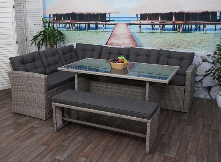 Graues Polyrattan-Lounge-Set bestehend aus Ecksofa, Esstisch mit Glasplatte und Sitzbank inklusive dunklen Polsterkissen.