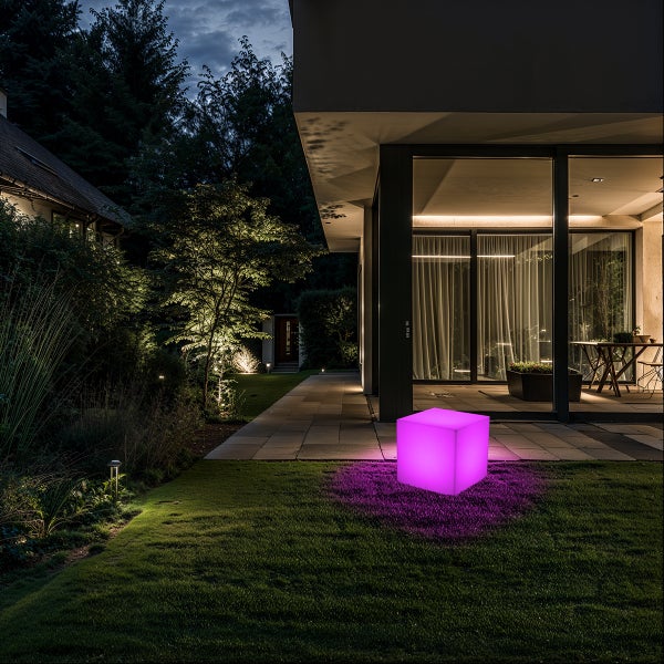 Violetter LED-Würfel leuchtend auf Rasenfläche in modernem Garten bei Nacht, neben Haus mit Glasfassade und Steinweg.