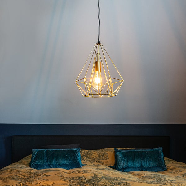 Goldfarbene geometrische Pendelleuchte über einem Bett