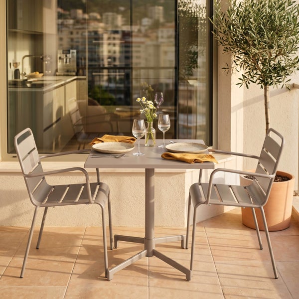 Modernes Balkonset aus Metall mit einem quadratischen Tisch und zwei Armlehnenstühlen auf einer sonnigen Terrasse.