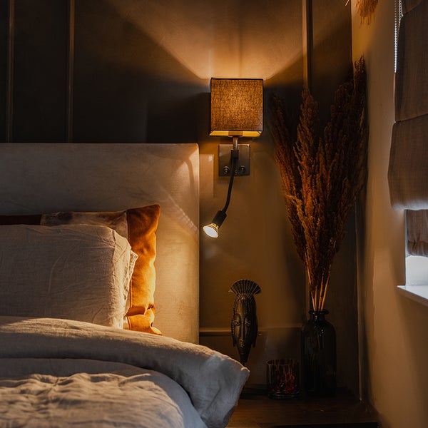 Schlafzimmer mit Bett, Nachttisch, Wandleuchte und Dekorationsgegenständen