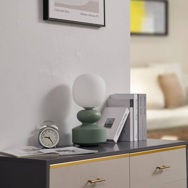 Dekorative Tischleuchte in Grün mit Uhr und Büchern auf einer Kommode