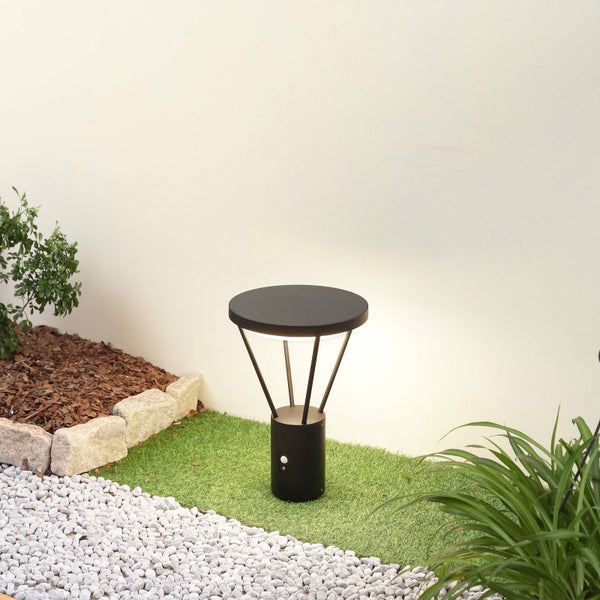 Moderne schwarze Wegeleuchte mit Bewegungsmelder im Garten auf Kunstrasen neben weißen Kieselsteinen.