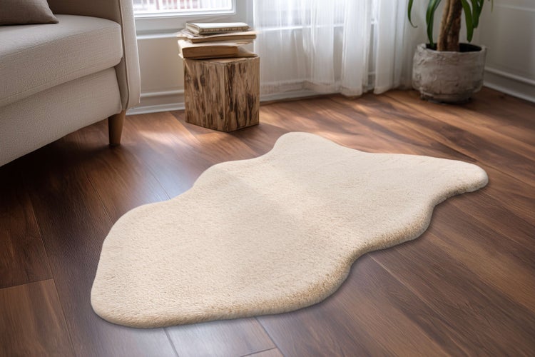 Beiger Webpelz Teppich in organischer Form auf dunklem Holzboden in einem hellen Wohnzimmer.