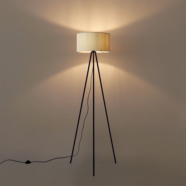 Dreibein-Stehlampe mit schwarzem Metallgestell und zylinderförmigem Stoffschirm in Beige, eingeschaltet.
