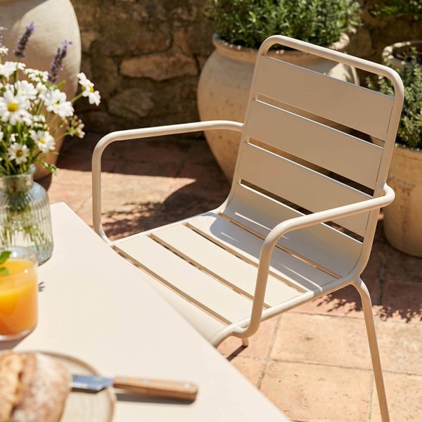 Gartenstuhl mit Armlehnen aus Metall im Latten-Design auf einer Terrasse neben einem Tisch mit Pflanzen.