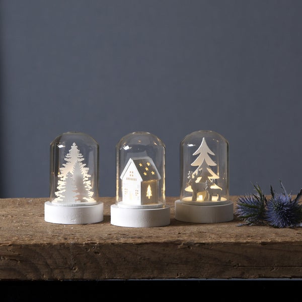 Drei dekorative Weihnachtskugeln mit Baum, Haus und Rentier auf einem Holztisch.