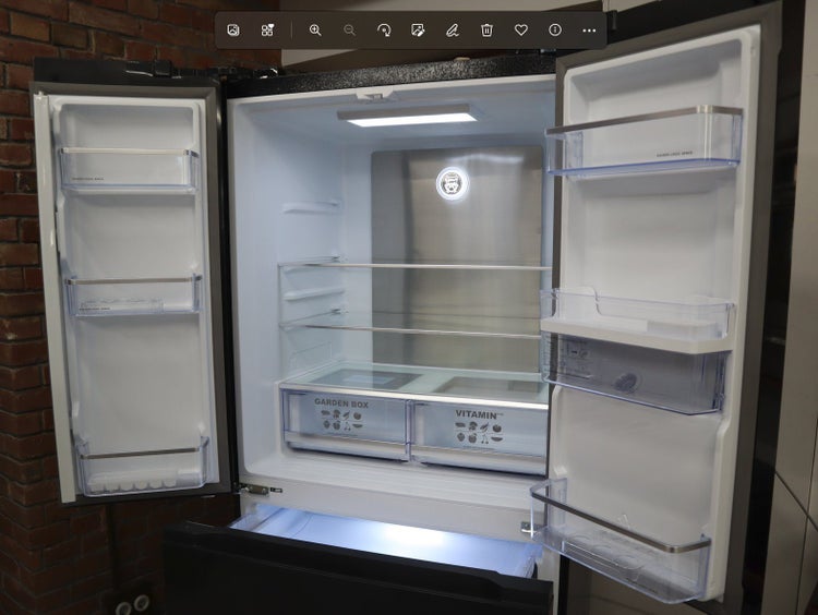Geöffneter Kühlschrank mit Doppeltüren und unterem Gefrierfach, ausgestattet mit Glasablagen sowie speziellen Fächern für Obst und Gemüse.