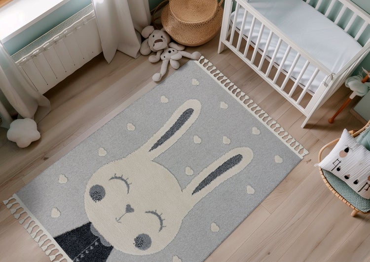 Kinderteppich mit Hasenmotiv und Quasten in einem freundlich eingerichteten Babyzimmer mit Holzboden und Gitterbett.