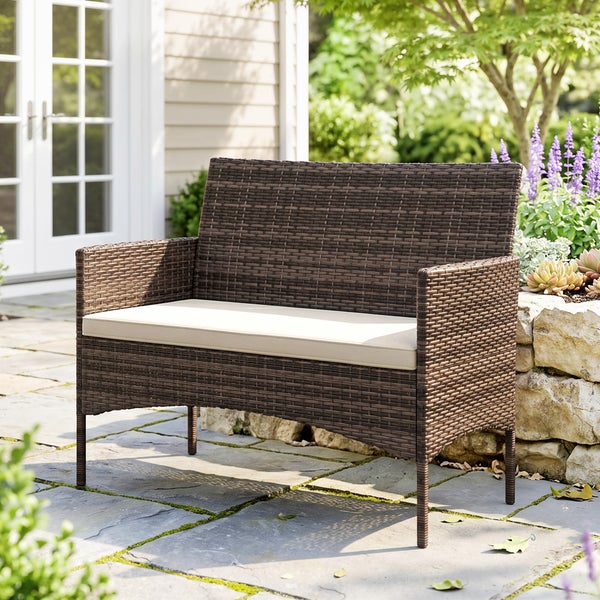 Zweisitzer Gartenbank aus Polyrattan-Geflecht mit Sitzpolster auf einer Steinterrasse in einem hellen Garten.