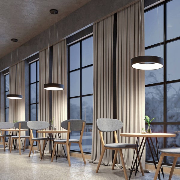 Moderne ringförmige LED-Pendelleuchten in einem hellen Esszimmer mit großen Fenstern, beigen Vorhängen und grauen Stühlen.