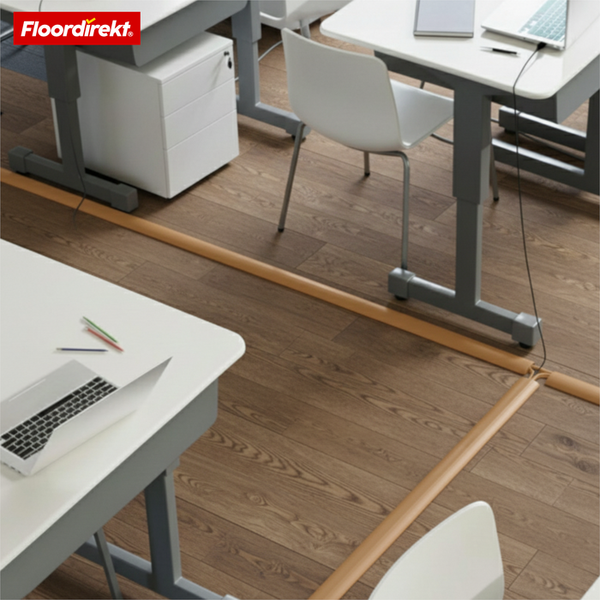 Floordirekt Logo. Eine Kabelbrücke auf einem Boden in Holzoptik in einem Büro mit Schreibtischen und Stühlen für sicheres Kabelmanagement.