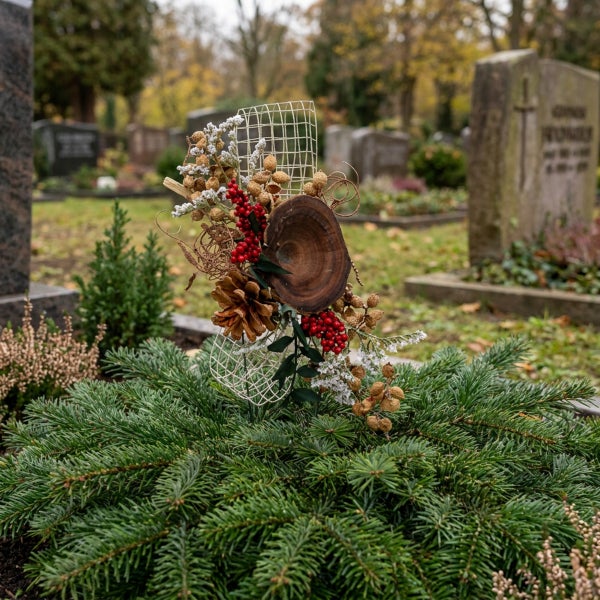 Grabgesteck aus Tannenreisig mit einer Dekoration aus Holzscheibe, Zapfen und roten Beeren auf einem Friedhof