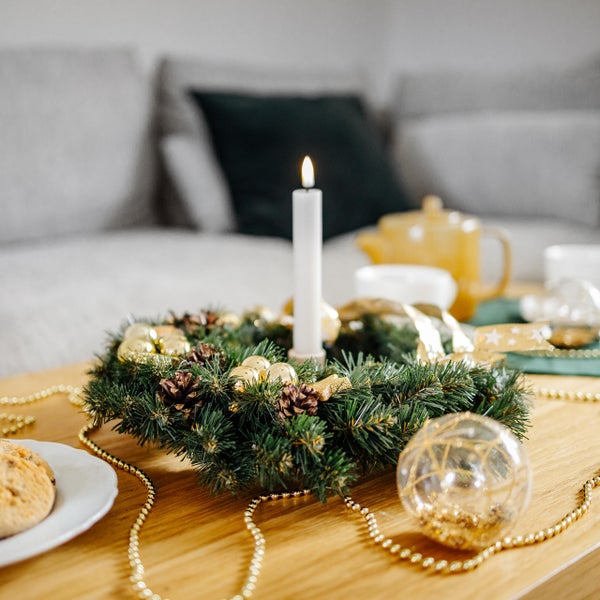 Dekorierter Weihnachtskranz mit goldener Schleife, Kugeln und Zapfen sowie eine Weihnachtssocke mit Rentier-Motiv an einer Garderobe aus Holz.