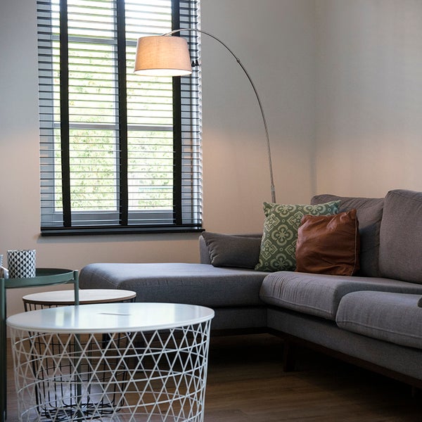 Wohnzimmer mit grauer Couch, Stehlampe und Jalousien vor dem Fenster