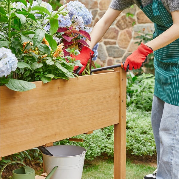 Eine Person bepflanzt ein Hochbeet mit verschiedenen Blumen.