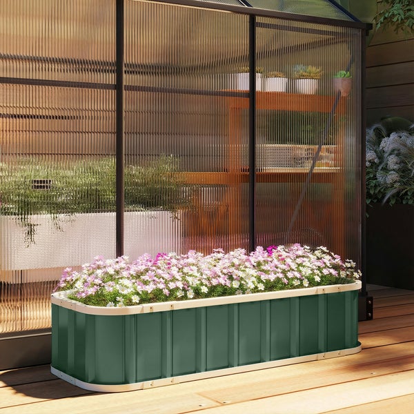 Niedriges Hochbeet aus grünem Metall mit cremefarbenem Rand, bepflanzt mit Blumen, auf einer Holzterrasse vor einem modernen Gewächshaus.