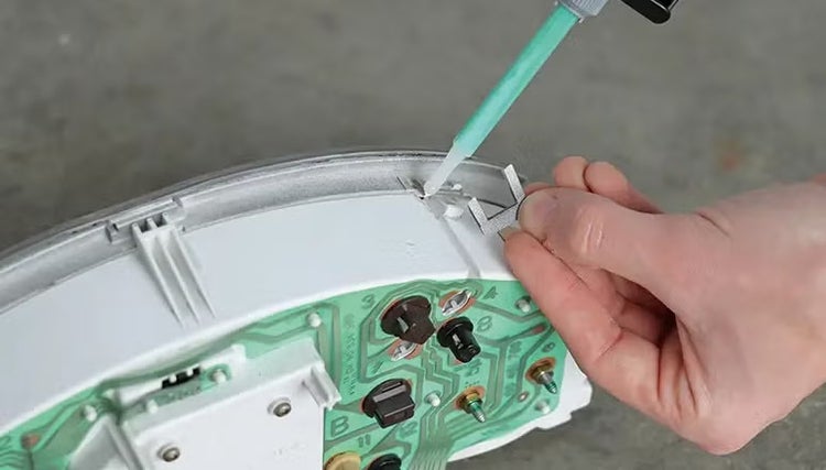 Hand beim Auftragen von Klebstoff mit einer Dosierspritze auf ein elektronisches Bauteil einer Tachoeinheit