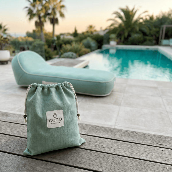 Hellgrüner COCO LOUNGE Beutel auf einem Holztisch mit einer hellgrünen Gartenliege und einem Swimmingpool im Hintergrund.
