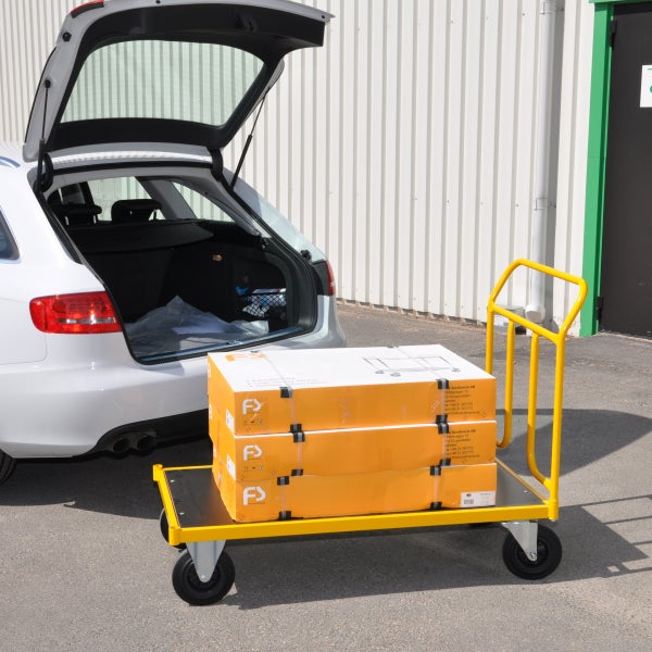 Gelber Transportwagen mit Paketen vor einem Auto