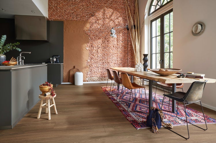 Moderne Küche mit Essbereich und rustikaler Backsteinwand, Holzesstisch, Metallstühlen und Boden in Holzoptik in einem hellen, weitläufigen Raum.