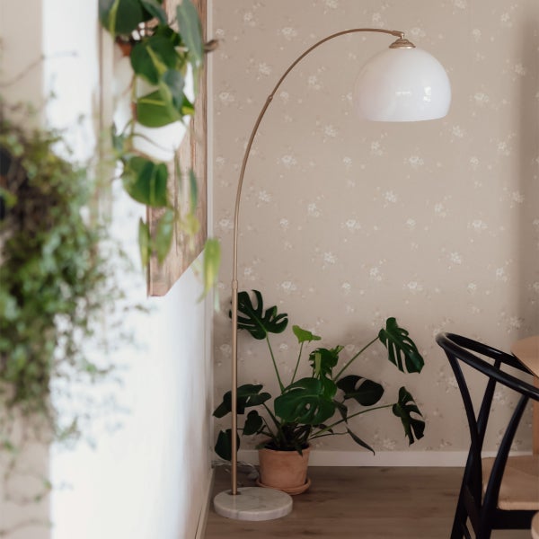 Bogenlampe mit weißem Schirm, Zimmerpflanze im Topf und Stuhl im Zimmer.