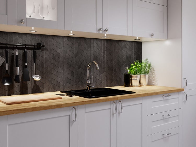 Moderne Küche mit Arbeitsplatte aus Holz, schwarzer Spüle, Chromarmatur, Rückwand mit dunkelgrauen Chevron-Fliesen und hellgrauen Schränken.