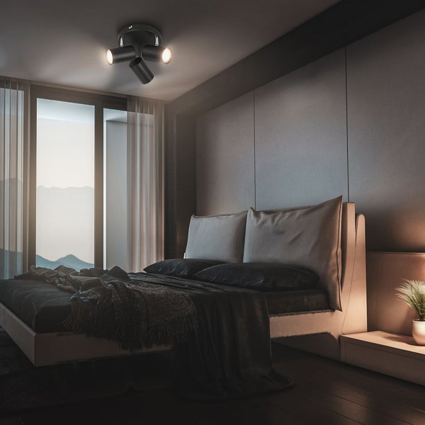 Dreiflammiger Deckenstrahler in einem modern eingerichteten Schlafzimmer mit dunklen Textilien und Panoramablick auf Berge.