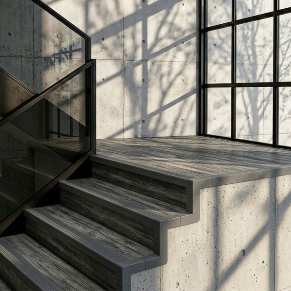 Moderne Treppe in Holzoptik mit Treppenkantenprofilen vor einer Sichtbetonwand, Glasgeländer und Sprossenfenster.