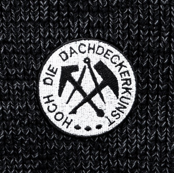 Rundes besticktes Abzeichen mit dem Zunftzeichen der Dachdecker und dem Text Hoch die Dachdeckerkunst auf Strickgewebe.