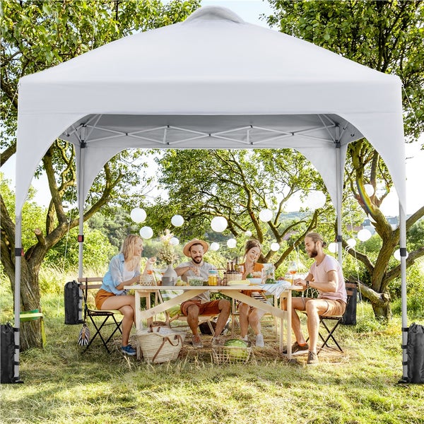 Szene im Garten mit einem weißen Faltpavillon und einer Gruppe von Personen, die an einem Holztisch sitzen.