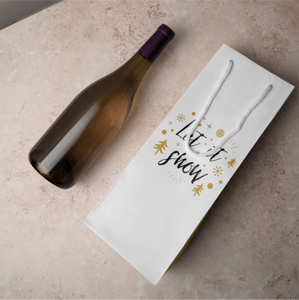 Weinflasche neben Geschenktasche mit Aufschrift Let it snow