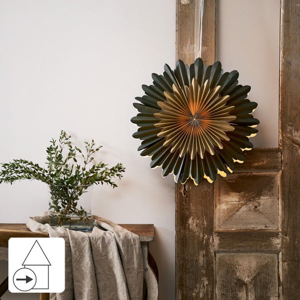 Dekorative Papiersternleuchte hängt an einer Holztür, Tisch mit Blumenvase und Stoff im Hintergrund.