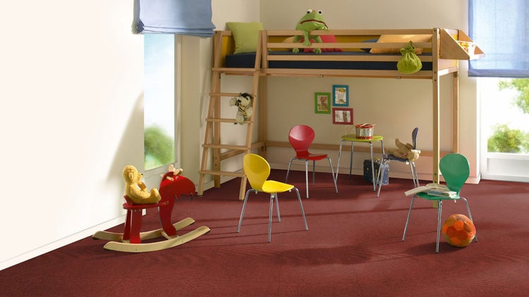 Helles Kinderzimmer mit rotem Teppichboden, einem Hochbett aus Holz, bunten Stühlen und einem roten Schaukelpferd.