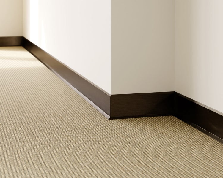 Detailansicht eines Raumes mit Teppichboden und dunklen Fußleisten.