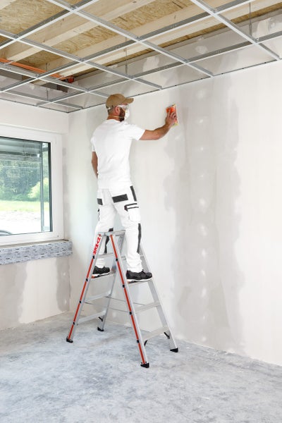 Mann schleift Wand auf Leiter in einem Raum mit Deckenkonstruktion