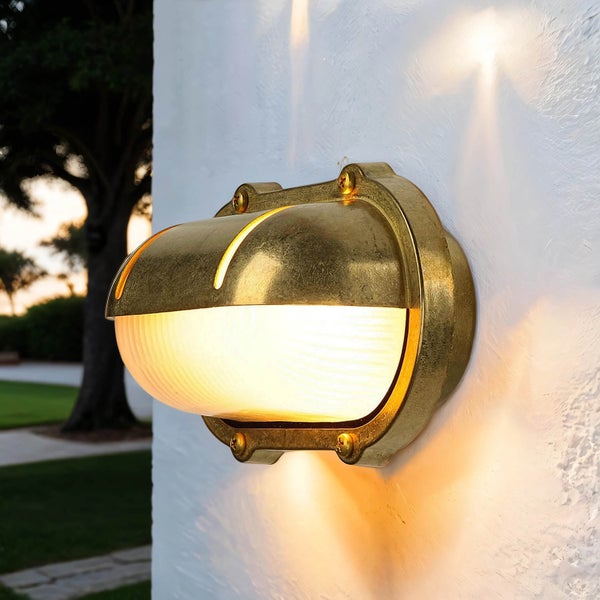Beleuchtete messingfarbene Außenleuchte an einer Fassade.